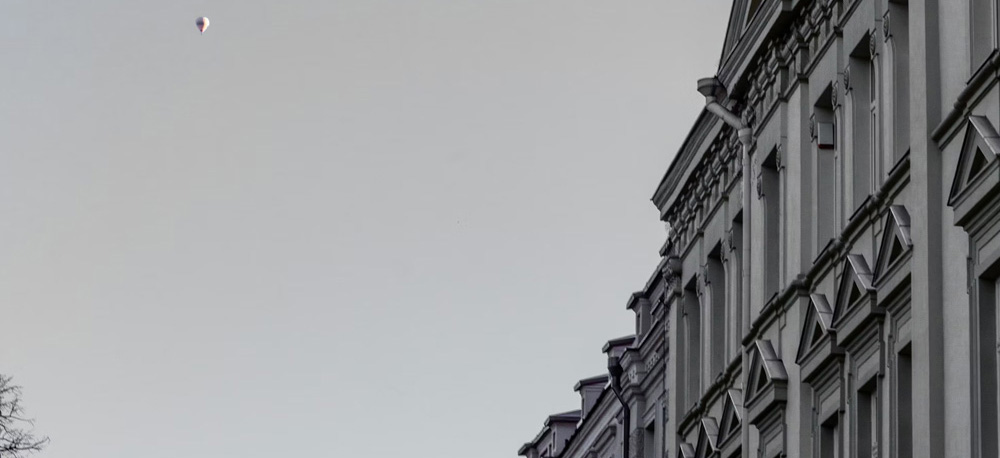Reihe von mehrstöckigen Altbauten mit Fassadendetails, darüber ein einzelner Heißluftballon am Himmel.